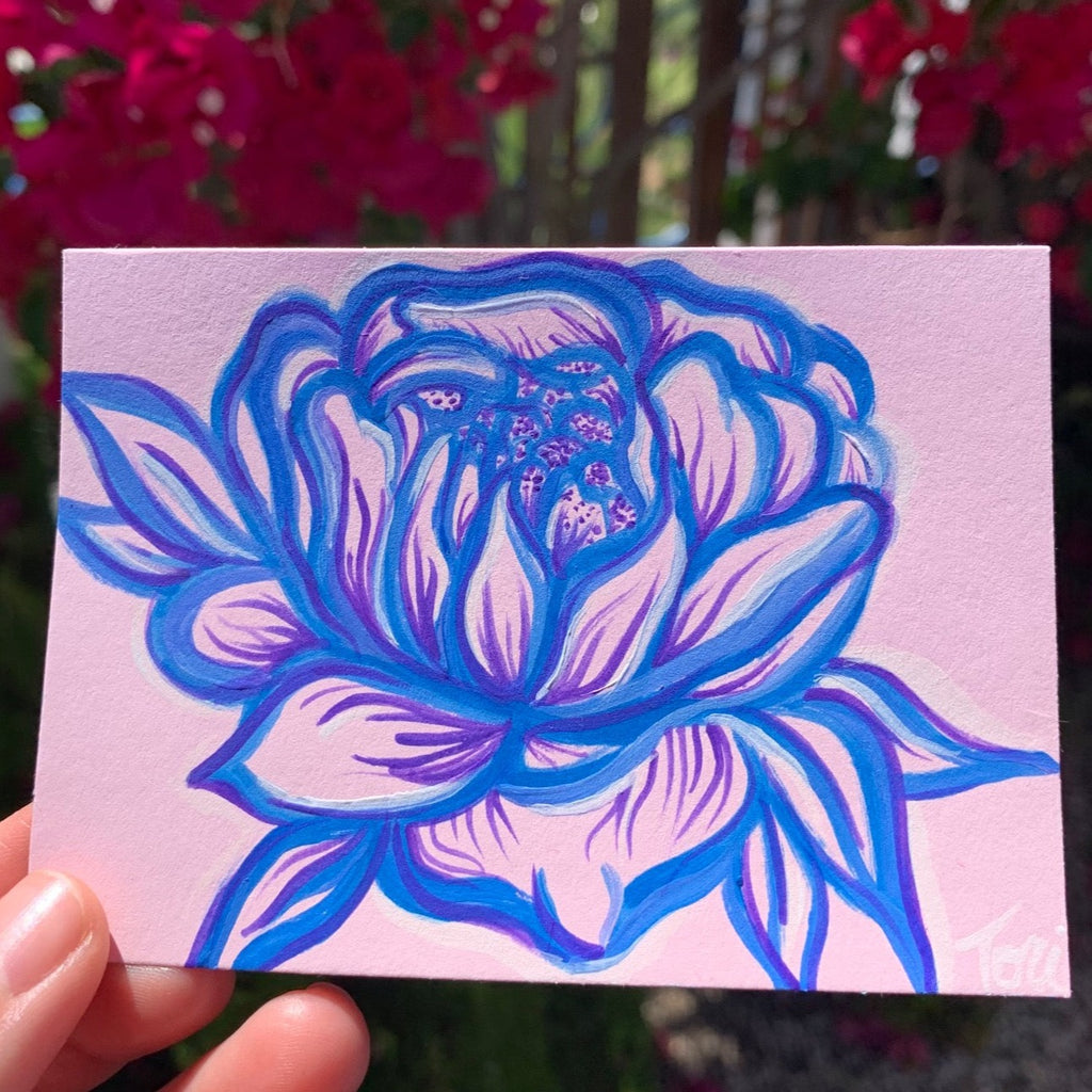 peony flower painted with acrylic paint in a royal blue color with violet purple and white accents on a pastel baby pink piece of paper.