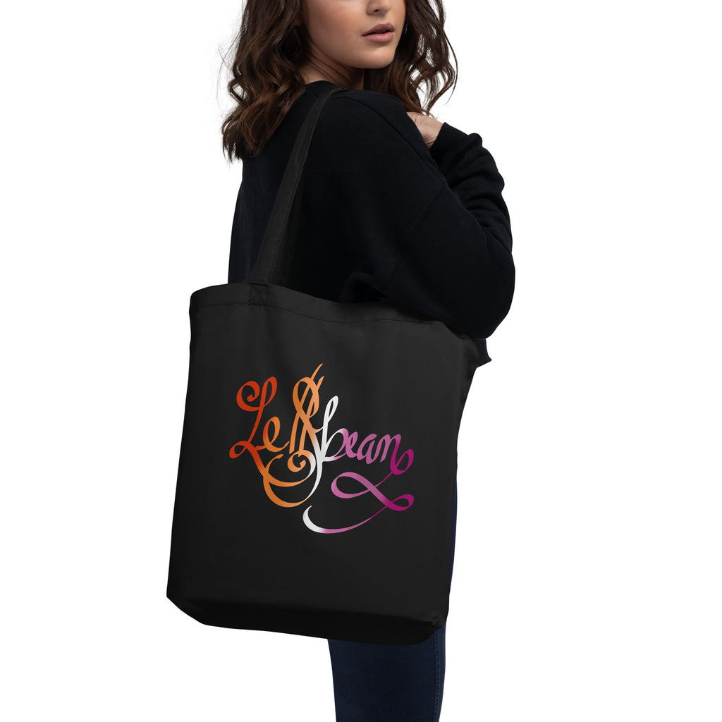 eco-friendly tote bag in black with Le$bean cursive calligraphy lettering in the colors of the lesbian flag (red, orange, white, pink & magenta). lgbtqia+ sapphic inspired art design for sustainable fashion