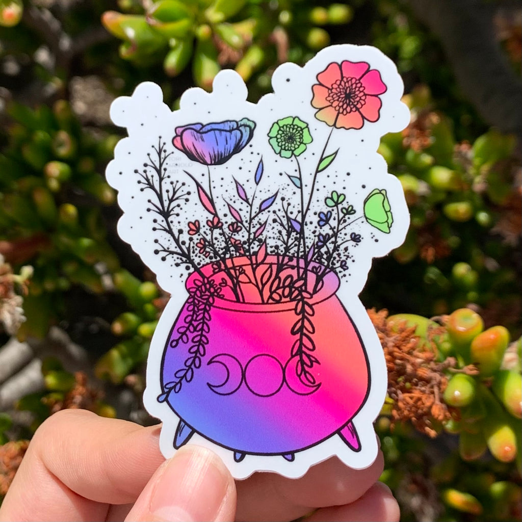 this coloful rainbow sticker has a witch's cauldron with the triple moon goddess symbol on it and multi-colored flowers growing out of it.